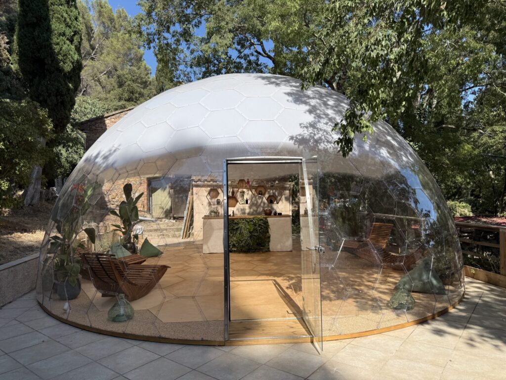 透明ガラスドーム「AURA DOME」のエントランス。ホテル、グランピング施設、リゾート、商業施設、カフェ、イベントスペースなど幅広い用途に対応する全天候型ドーム建築。