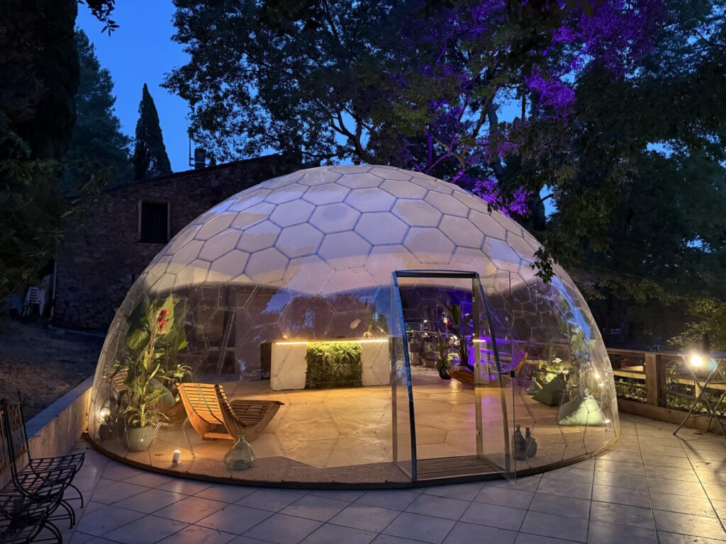 夜間にライトアップされた透明ガラスドーム「AURA DOME」の外観。ホテルやリゾート施設のラウンジ・イベントスペースとして活用できる全天候型ドーム建築。